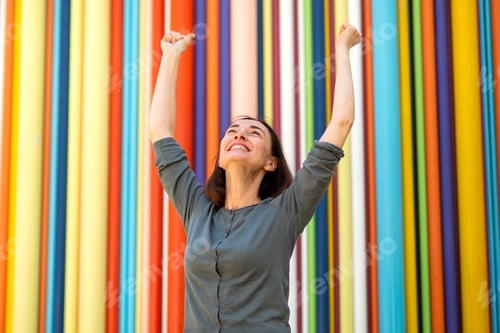 Preview: cheerful middle age woman against colorful background with arms in air
