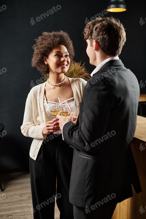 Preview: happy curly african american woman looking at boyfriend while holding glass of wine during date