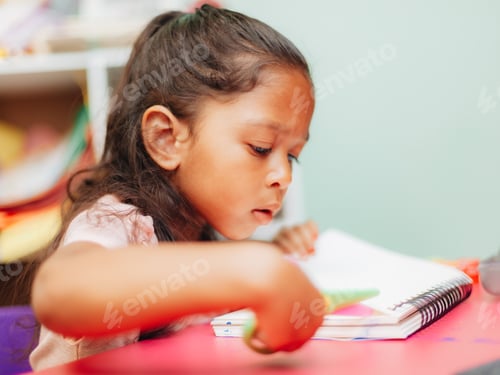 Preview: Diverse pre school girl at home doing arts and crafts, cutting out painting from book