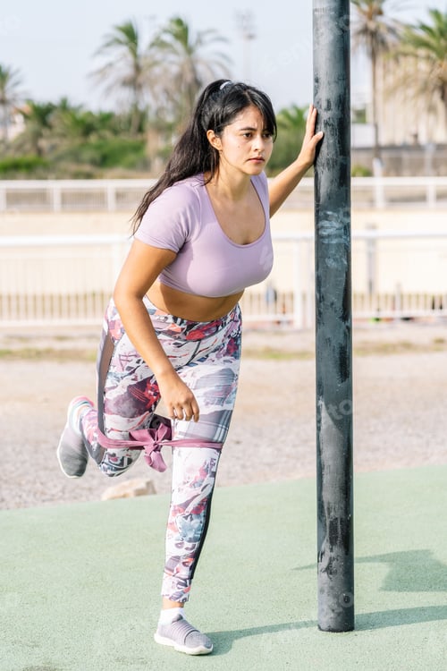 Preview: Latin woman doing exercise for legs with fitness elastic gums in a calisthenic park