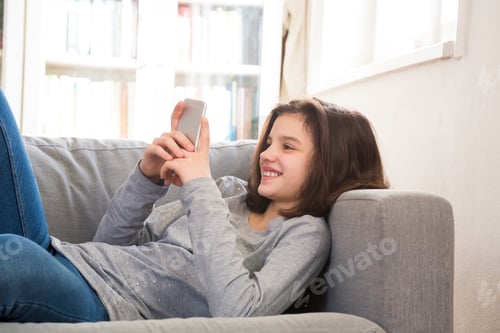 Preview: Teenage Girl Using Smartphone Reclining on Sofa Indoors