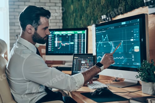 Preview: Concentrated young modern man in formalwear working using computers while sitting in the office