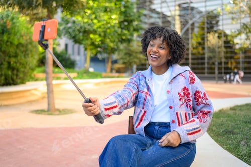 Preview: Young woman vlogging outdoors with selfie stick and smartphone