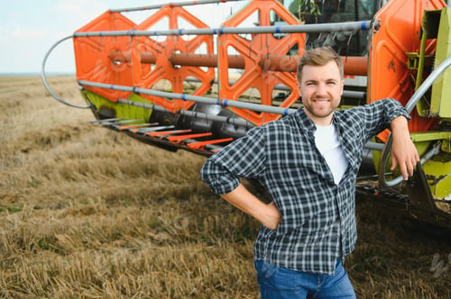 Preview: Happy farmer proudly standing in a field. Combine harvester driver going to crop rich wheat harvest