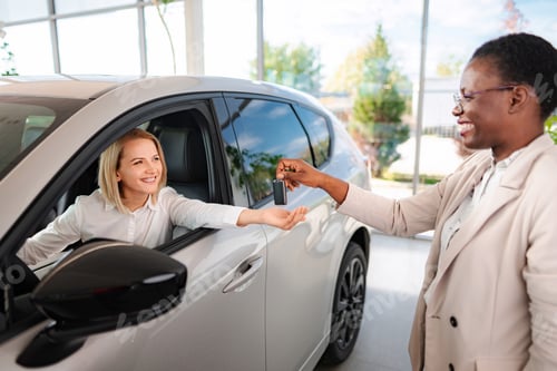 Preview: Woman receiving car key from saleswoman at dealership