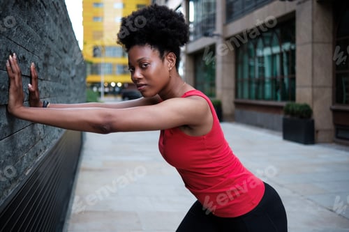 Preview: Portrait of young fit black woman stretching against a wall.