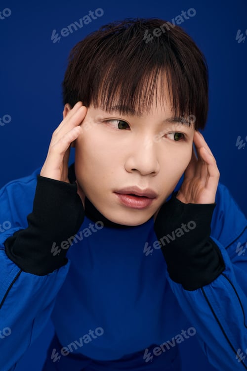 Preview: Young handsome Asian man expressing deep thoughts in a vibrant blue setting