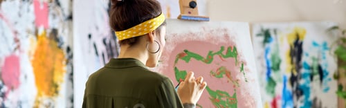 Preview: Back view of young female artist creating abstract painting, standing in living room at home