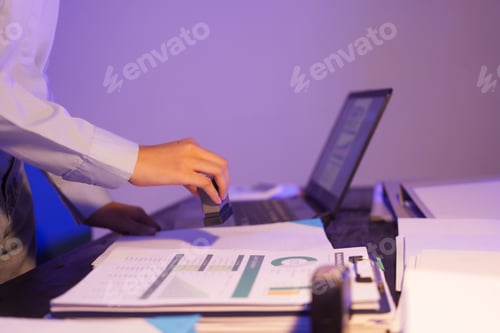 Preview: An Asian woman is working overtime at her desk in the office,busy viewing documents her notebook