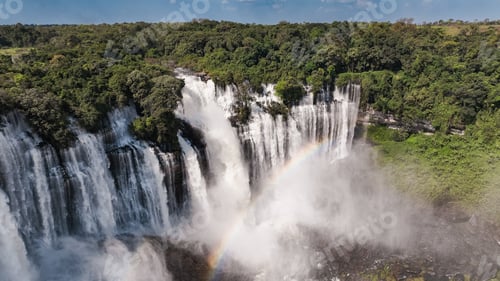 Preview: Kalandula Waterfall cascades in Angola with vibrant rainbow above lush greenery during daylight