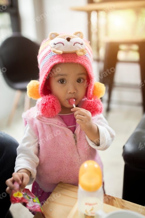 Preview: A portrait of a cute little girl in a pink dress eating a bright red Lollipop