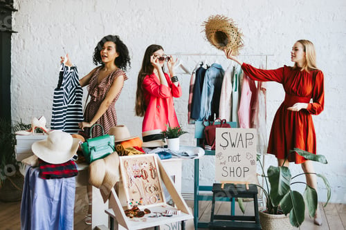 Preview: three young woman female caucasian and african students at swap party try on clothes, bags, shoes an