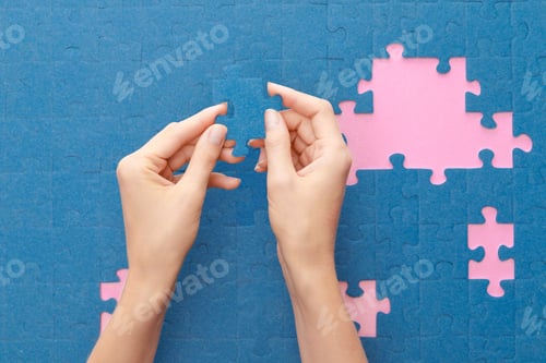 Preview: cropped view of woman holding blue jigsaw puzzle on pink background
