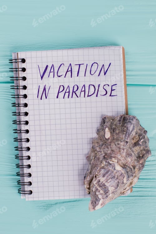 Preview: Close-up notepad with words vacation in paradise and tropical sea shell on blue desk.
