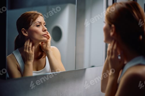 Vista previa: Mujer de mediana edad mirándose en un espejo en el baño.