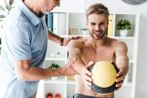 Preview: cropped view of bearded doctor standing near patient working out with ball