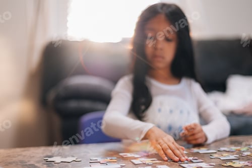 Preview: Diverse toddler girl at home with pretty black hair entertaining herself by solving simple puzzle