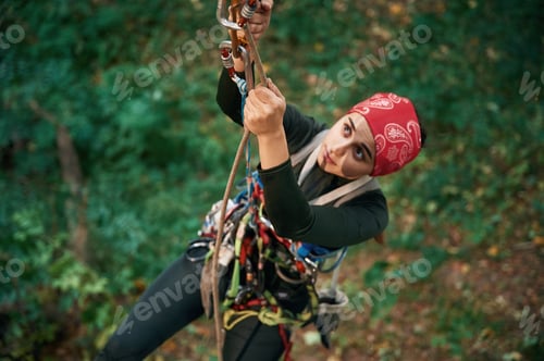 Preview: Focused on the climbing up. Woman is in the forest, using the safety equipment