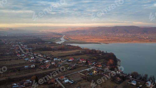 Preview: Aerial view of a river next to countryside buildings under dense and fluffy clouds