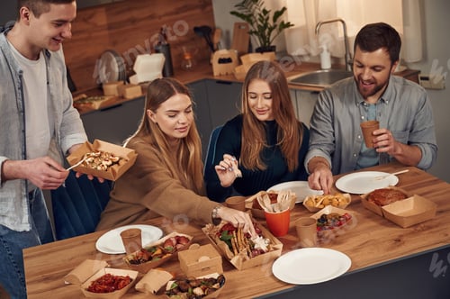 Preview: By the table. Friends are sitting indoors at home and eating together