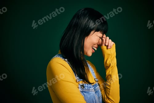 Preview: Side profile of an Asian woman, standing and laughing, posing on the green background.