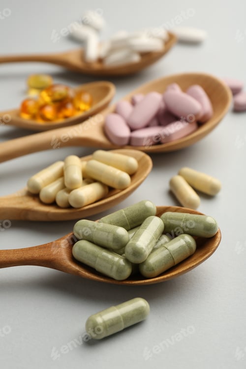 Preview: Different vitamin pills in spoons on light grey background, closeup. Health supplement