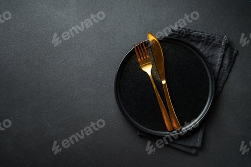 Preview: Black plate with golden cutlery. Flat lay at black background.