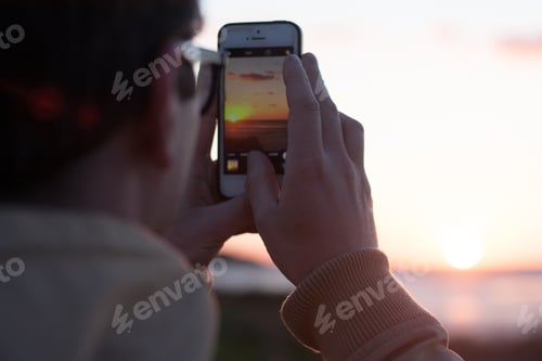Preview: A man takes a picture of the sunset on his phone