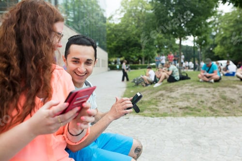 Preview: Two friends sharing a fun moment on a smartphone in a park