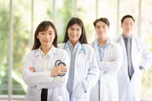 Preview: Group of Asian doctors team portrait standing with colleagues in background.