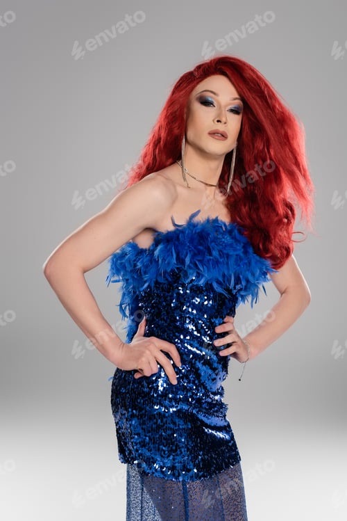 Preview: Elegant drag queen with red wig and dress posing isolated on grey