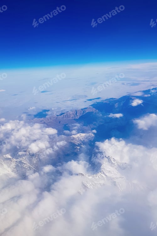 Preview: View from window of plane to blue sky and snowy mountain peaks in white clouds