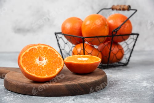 Preview: A metallic black basket full of juicy orange fruit on stone background