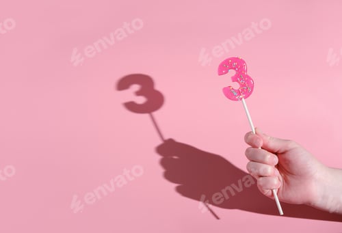 Preview: girl's hand holding a number 3 shaped lolipop. anniversary or birthday selebration. kids party