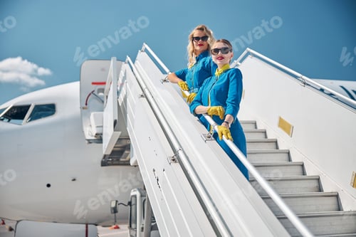 Preview: Beautiful stewardesses standing on airplane stairs under blue sky