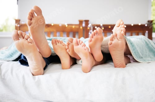 Preview: Feet of family lying in bed. Closeup of feet of parents and children in bed. Family relaxing in bed