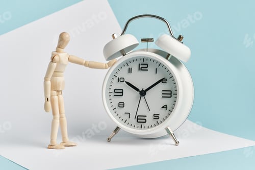 Preview: Wooden man stands with his hand on the alarm clock. Time management, waiting, punctuality.