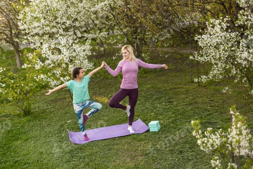 Preview: Young sports mother doing physics exercise outdoors in garden near her daughter. Healthy lifestyle.