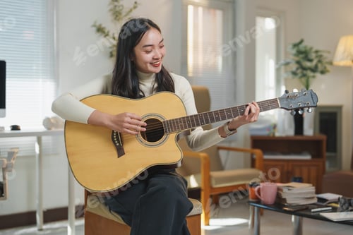 Vista previa: Young asian woman playing acoustic guitar at home