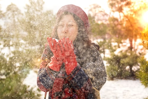 Preview: Happy Asian woman picked up snow in her hands and blows on it in winter snowy day. Hair and hat in s
