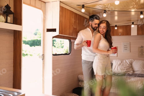 Preview: Happy young couple with cups in trailer. Camping vacation