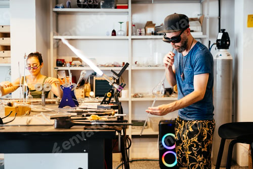 Aperçu: Young Man Skillfully Blowing Glass in a Creative Studio Setting