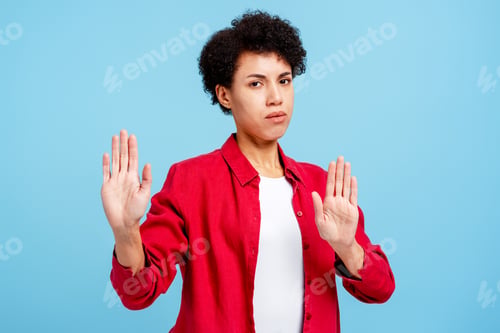 Preview: Serious woman wearing pink shirt showing stop sign looking at camera isolated on blue background
