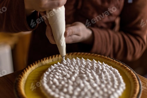 Preview: hands of a man using a piping/icing bag to frost a lemon pie