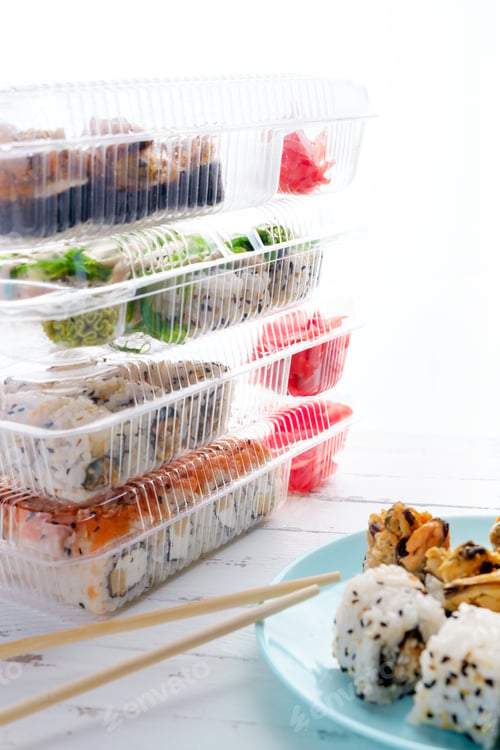 Preview: Stack of plastic boxes with sushi rolls, a plate with sushi on table. Food delivery