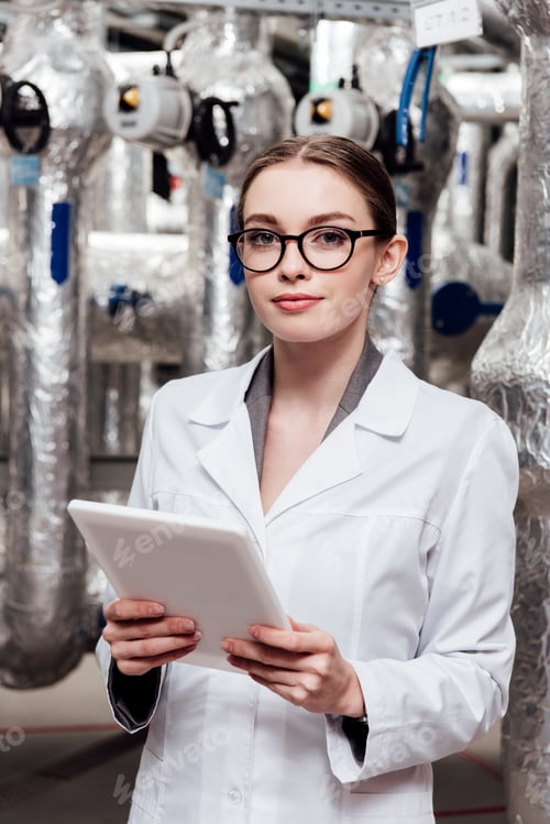 Preview: attractive engineer in white coat and glasses holding digital tablet near air compressed system