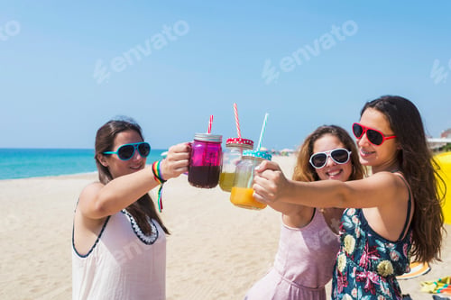 Preview: group of happy young women or female friends toasting non alcoholic drinks on summer beach