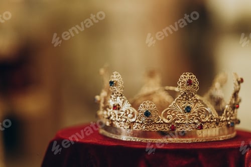 Preview: golden crown with gemstones on red napkin on altar in church