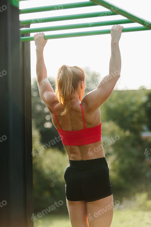 Preview: Woman building strength doing pull ups outdoors