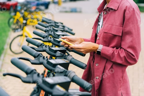 Preview: An unrecognizable cropped woman rents an electric scooter using an app on her phone.